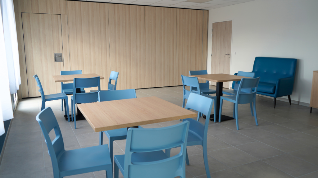 Salle de convivialité avec des tables, des chaises et un fauteuil.